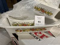 Overview of two vintage Corning Ware baking dishes with fruit pattern, one long rectangular and one shorter, both with clear glass lids, wrapped in bubble wrap.