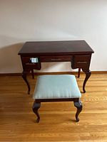 Front view of the antique cherrywood vanity with all three drawers closed and the light teal cushioned stool in front.