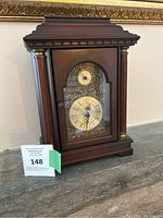 Front view of the wooden mantel clock with decorative clock face and side columns with gold accents.