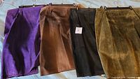 Four suede skirts laid out side by side in purple, brown, black, and olive green colors.