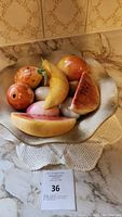 Marble fruits and eggs in a scalloped edge marble bowl on a crocheted doily on countertop, showing complete set from side angle.