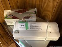 Photo of FoodSaver vacuum sealer machine with a green label and attached white cord, box of vacuum storage bags in background with some bags pulled out.