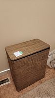 Full view of the rectangular brown wicker style laundry basket with closed hinged lid.
