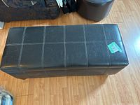 Top view of rectangular black leather storage bench showing stitched pattern and minor scuffs.