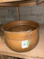 Massive vintage copper planter placed on wooden shelf, showing the round shape, rim detail, and attached metal loop for hanging.