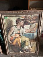 Photo of framed art print showing seated figure reading a book with cherubs above, framed in a large, ornate wood frame.