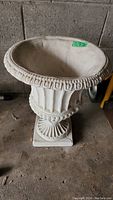 Photo of a large outdoor concrete planter urn with a thick ornate rim, fluted base, and square pedestal bottom.