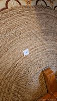 Partial angled view of round braided rug showing natural fiber braiding and furniture leg on top.