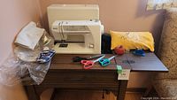 Wide view showing Kenmore sewing machine on wood table with sewing accessories including scissors and pincushion laid out on the table.