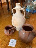 The three terracotta jugs displayed on a wooden floor showing their shapes and surface markings.