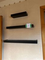 Front view of three black floating shelves mounted on wall of varying lengths.