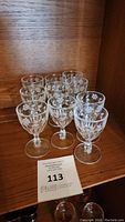 Set of 10 vintage wine glasses arranged on a wooden shelf, showing etched grape patterns on clear glass bowls.