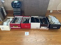 Wide shot of six pairs of women's shoes in original boxes on a wooden floor with a CD player and chair in background.