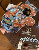 Overview showing fabric table runner, placemats, napkins, lacquer box, porcelain plate, place card holders, chopstick holders, chopsticks and fondue forks.