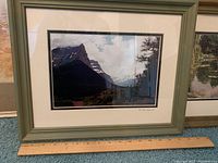 Framed mountain landscape photograph with mat and greenish-gray frame, showing a rugged mountain under partly cloudy sky