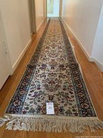 Full length view of the carpet runner placed in hallway with fringed ends and bordered floral pattern in blue, red, and cream.