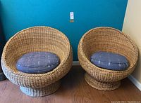 Two wicker lounge chairs side by side with blue cushions against a teal wall