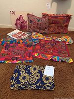Group photo of two mola blouses, two pillow covers, folded fabric, and a photo on backing arranged on carpeted floor