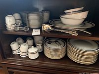 Shelved view of plates, bowls, cups, crystal tool rest, silver salad tongs and candle snuffer.