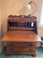 Front view of wood secretary desk with flip down portion opened, displaying interior compartments, built-in lamp on top with blown glass paperweight.