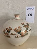 Front view of the bowl-shaped Japanese ceramic vase with floral and gilt design on a cream background.