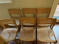 Six matching light oak wood kitchen chairs with rattan seats and backs, arranged in two rows of three.