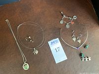 Full view of jewelry lot showing necklaces, earrings, pin, bracelet, charms arranged on a brown surface.