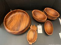 Photo showing 8 oblong teakwood salad bowls, one large round serving bowl, and one pineapple silhouette bowl all with natural wood finishes.