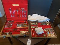 Two open wooden chests showing complete bronze flatware set and white linen napkins on table.