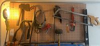 Wide shot of the pegboard showing multiple hand tools mounted including saws, mallet, crowbar, clamp, work light, and pulley system.