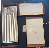 Three vintage electric warming trays on black background showing decorative warming surfaces and wooden handles.