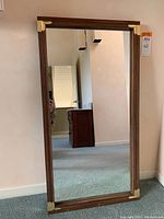 Full view of large rectangular mirror leaning against wall showing dark wood frame and clear mirror surface.