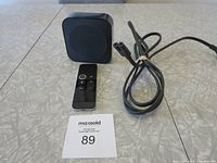 Top and front view of Apple TV box, remote control, and power cable on table.