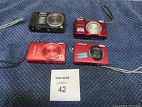 Front view of four compact cameras showing brand logos, lens rings and zoom markings