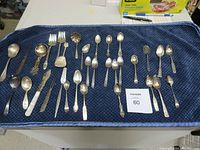 Full spread of assorted silver plated cutlery on blue fabric, showing variety of forks, knives, spoons, and serving pieces.