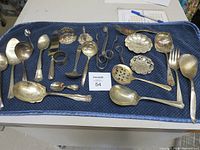 Overview of assorted silver plate spoons and serving utensils laid on a blue cloth.
