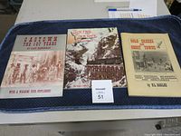 Three vintage historical books placed on a blue cloth with MaxSold tag number 51. Titles visible: Gastown the 107 Years, White Pass and Yukon Route, Gold Rush Ghost Towns.