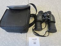 Black Nikon-branded carrying case with shoulder strap and Nikon Action binoculars placed next to it on a surface.
