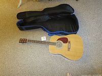 Full view of the Burswood acoustic guitar next to its soft case on a carpeted floor.