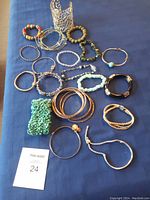 Top view of 18 assorted costume jewelry bracelets including metal bangles and various beaded designs arranged on a blue background.