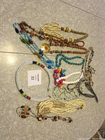 Top-down photo of assorted beaded costume necklaces and jewelry pieces laid on a grey patterned floor.