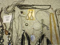 Photo showing an assortment of costume jewelry including necklaces, earrings, rings with varied bead styles, metal tones, and a pearl-studded compact accessory.