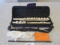 Photo showing the flute inside its black padded carrying case along with white gloves, orange cleaning cloth, and cleaning rod.
