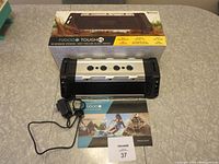 Photo of the speaker with the charging cable, user manual, and lot tag in front, all items placed on table surface.