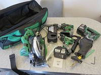 Full set of green and black Hitachi power tools laid out with charger, batteries, and duffle bag on table.