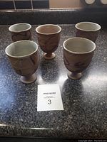 Five Japanese pottery cups arranged on black countertop, showing shape and size relative to sale lot card.