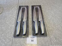 Two sets of Basque cutting utensils each with two knives in blister packaging, one serrated and one straight-edged.