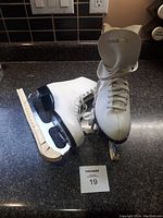 Pair of white Bauer figure skates with blades and attached skate guards on black counter