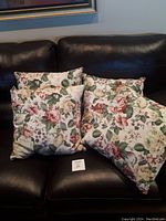 Set of four floral outdoor cushions arranged on a black leather couch.