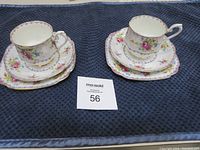 Two sets of Royal Albert china teacup, saucer, and dessert plate arranged side by side on a dark textured cloth.